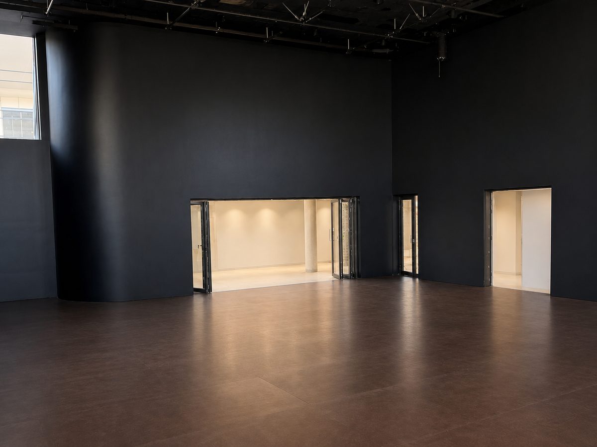 Performance theatre with a dark sprung floor and Weathertex overlay, opening to a lit foyer